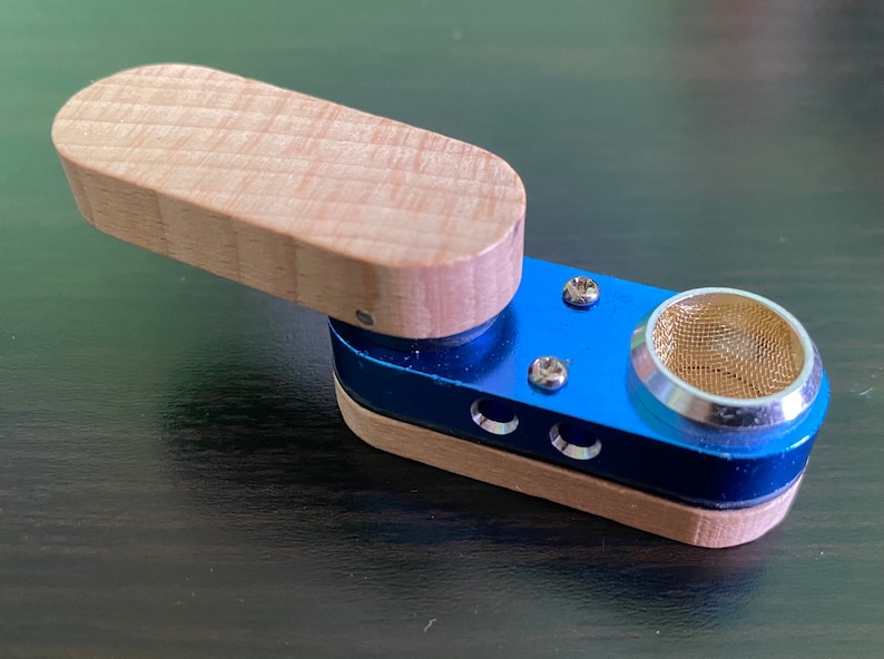 May include: A small, blue and wood smoking pipe with a metal screen. The pipe has a removable wooden lid.