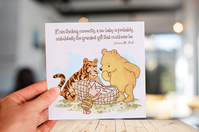 K&ouml;nnte beinhalten: Eine Karte zum Thema Winnie Puuh mit einem Zitat aus dem Buch: "Wenn ich richtig liege, ist ein neues Baby wahrscheinlich das gro&szlig;artigste Geschenk, das man sich vorstellen kann." Die Karte zeigt Winnie Puuh, Tigger und Ferkel, die ein Baby in einem Korb betrachten.