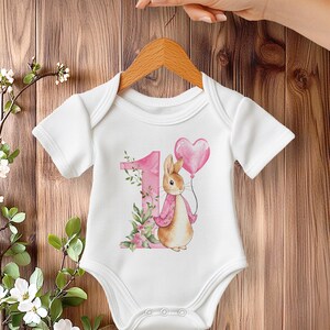 Watercolor Peter Rabbit birthday PNG clipart set with pink jacket bunny, heart balloon, greenery and floral number 1, 2 and 3 designs, shown on a baby bodysuit mockup.
