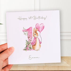 Watercolor Peter Rabbit birthday PNG clipart set with pink jacket bunny, heart balloon, greenery and floral number 1, 2 and 3 designs, shown on a baby bodysuit mockup.