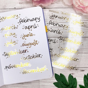 Könnte beinhalten: Goldfolien-Aufkleber mit den Monaten des Jahres in Kursivschrift. Die Aufkleber befinden sich auf einer transparenten Folie und sind zum Abziehen und Verwenden bereit.