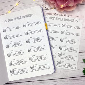 Pode incluir: Um caderno branco e uma folha de adesivos combinando com um design "Book Series Tracker". Cada rastreador apresenta espaços para o título da série, revisão e classificação, com um ícone de pilha de livros. O design é em tinta preta.