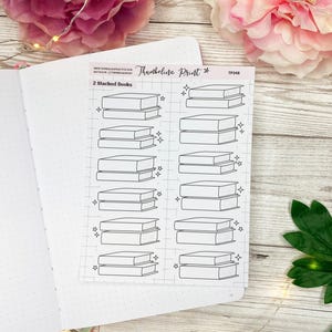 May include: A sheet of printable planner stickers featuring 10 illustrations of stacked books. The stickers are black and white and have a simple, minimalist design. The text "2 Stacked Books" is at the top of the sheet.