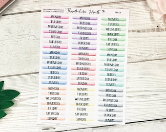May include: A sheet of colorful watercolor stickers with the days of the week written on them. The stickers are in three columns, each with a different color scheme. The colors are pink, purple, and green.