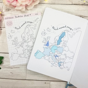 Peut inclure: Un carnet et une feuille de papier quadrillé avec une carte de l'Europe, avec des reflets bleus à l'aquarelle sur les pays. Le texte "travel around europe" est écrit en cursive. Le carnet a un ruban bleu clair.
