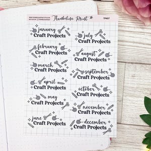 Pode incluir: Uma folha de adesivos de planejador mensal com um padrão de grade cinza e branco. Cada adesivo apresenta um mês do ano, o texto "Craft Projects" e uma variedade de ícones relacionados ao artesanato, incluindo tesouras, fio e lápis.