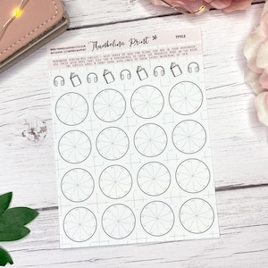 May include: A sheet of white planner stickers with black circular designs, each divided into segments. The sheet includes text and icons of books and headphones. The stickers are on a white wooden surface, with a pink wallet and a flower in the background.