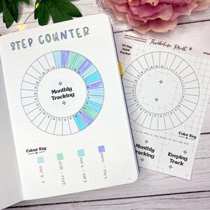 May include: Notebook open to a "Step Counter" design, with a circular "Monthly Tracking" chart and a separate "30 Day Habit Tracker" sheet. The design includes a colour key for step counts. Measurements are in steps.