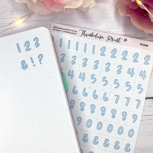 May include: A light blue sticker sheet with numbers and symbols, including the text "Thumbelina Print". A dotted notebook displays the numbers 1, 2, 3, and symbols. The stickers are for journaling and crafts.