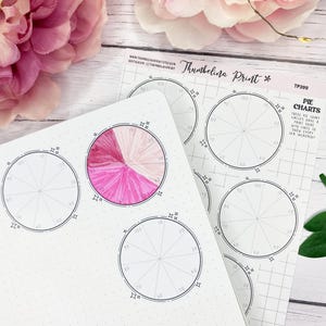May include: Notebook and paper sheets with pie chart templates. One chart is colored in shades of pink. The paper sheets have the text "Thumbelina Print" and "Pie Charts". The background includes pink flowers and green leaves.