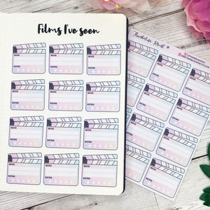 May include: A sheet of stickers with a clapperboard design. The stickers are pink, blue, and white with a watercolor effect. Each sticker has a space to write the name of a movie and a rating.