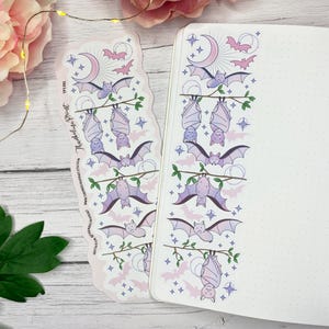 May include: A bookmark and a journal with a repeating pattern of bats, moons, and stars in shades of purple and pink. The bookmark has the text "Thunderbolt Print" and a website address. The journal is open to a blank page.
