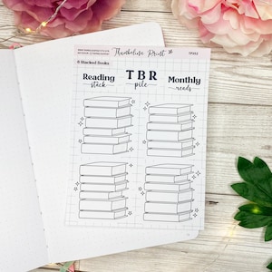 May include: A sticker sheet with six stacks of books, labeled "Reading stack", "TBR pile", and "Monthly reads". Each stack is outlined in black, with star accents. The sticker sheet is on a white notebook.