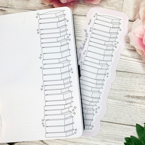 May include: A black and white illustration of a stack of books with star accents, next to a notebook. The illustration is also on a sticker with the text "TheWildestPrint". The notebook has a dotted grid pattern.