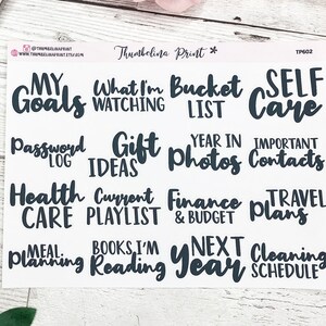 May include: A sheet of black and white planner stickers with various categories, including "My Goals", "What I'm Watching", "Bucket List", "Self Care", "Password Log", "Gift Ideas", "Year in Photos", "Important Contacts", "Health Care", "Current Playlist", "Finance & Budget", "Travel Plans", "Meal Planning", "Books I'm Reading", "Next Year", and "Cleaning Schedule".