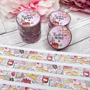 May include: Pink washi tape rolls with a repeating pattern of desserts and the text "Thumbelina PRINT". The rolls are stacked and arranged with a sheet of matching patterned stickers. The background includes pink flowers.