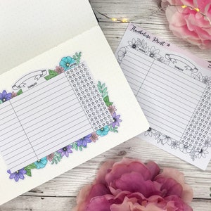 May include: A product review tracker sticker sheet featuring a floral border with blue, purple, and pink flowers. The sheet includes columns for product name, thoughts, and a star rating system. One sheet is placed inside a dotted journal.