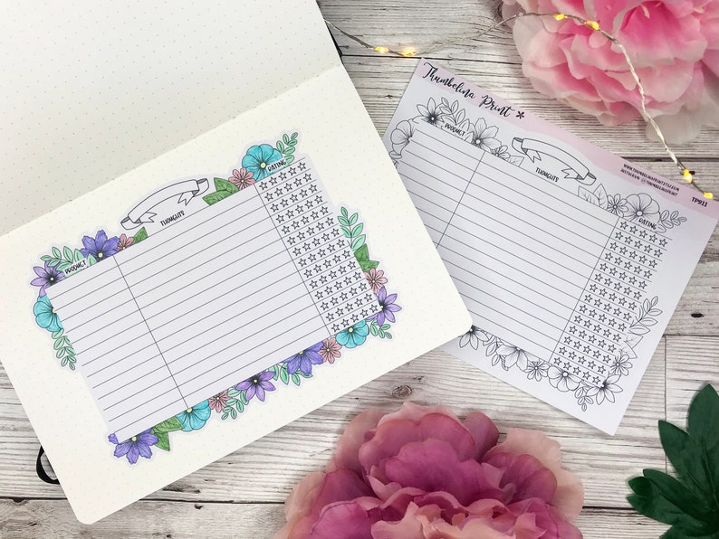 May include: A product review tracker sticker sheet featuring a floral border with blue, purple, and pink flowers. The sheet includes columns for product name, thoughts, and a star rating system. One sheet is placed inside a dotted journal.