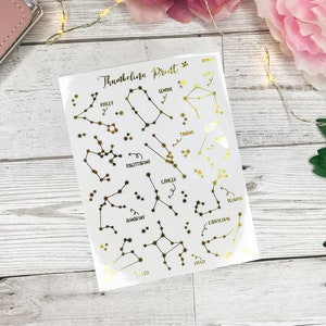 May include: A sheet of gold foil constellation stickers with the names of each constellation written in black. The constellations include Pisces, Gemini, Taurus, Sagittarius, Cancer, Aquarius, Capricorn, Virgo, and Leo.