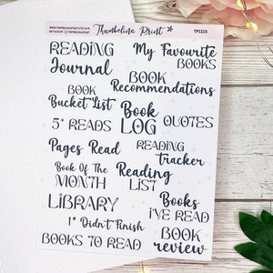 May include: A sheet of stickers with a pink background and black text. The stickers are for a reading journal and include titles like "Reading Journal", "Book Recommendations", "Book Quotes", "Pages Read", "Book of the Month", "Library", "Books I've Read", "Books to Read", and "Book Review".