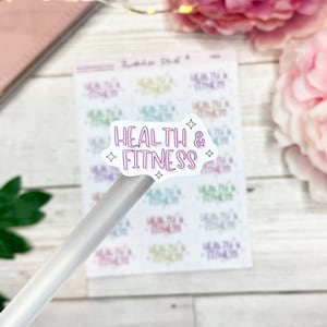 May include: A sheet of stickers with the words "HEALTH & FITNESS" in a bubble design, accented with stars. The stickers are in various colors, including purple, green, and blue. A pen rests on the sheet.