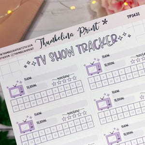 May include: A sheet of TV show tracker stickers with a light purple and white color scheme. The stickers feature a retro TV graphic, spaces for show and season, and a review section with stars. The text "TV SHOW TRACKER" is displayed.