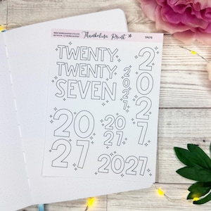 May include: A white sticker sheet featuring black outline text that reads TWENTY TWENTY SEVEN and various iterations of the number 2027, accented with small star symbols. The sheet is labeled Thumbelina Print and TP076 at the top edge.