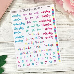 May include: A sheet of colorful planner stickers with days of the week, numbers 1-31, and phrases like "To Do List", "One Line A Day", "Monthly Overview", "Habit Tracker", "Goals", "Purchases", "Workout Tracker", and "Brain Dump".