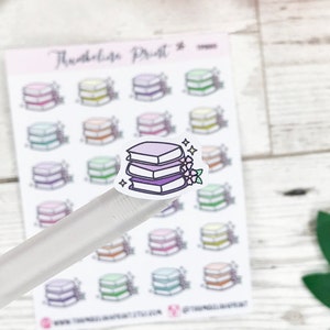 May include: A sheet of stickers featuring a stack of books with flowers. The stickers are in a variety of colours, including purple, pink, and blue. The sheet is labelled "Threaded Print".