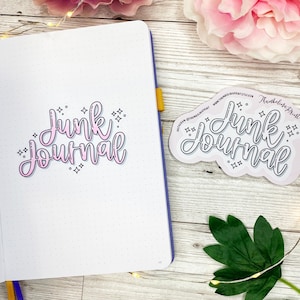 May include: A pink and white sticker with the text "Junk Journal" in a handwritten style. The sticker is surrounded by small stars.