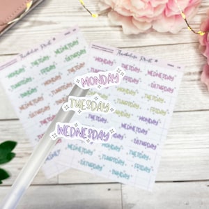 May include: Three clear stickers with the words "Monday", "Tuesday", and "Wednesday" written in different colors. The stickers have a sparkly design around the edges.