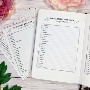 May include: A white notebook and several sheets of paper with the text "ONE COUNTRY, ONE BOOK - europe edition". The notebook and papers have a list of European countries with checkboxes. The image is on a light wood surface.