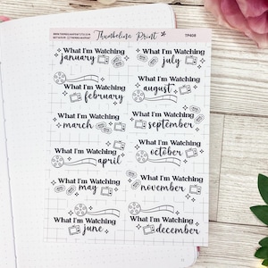May include: A sheet of black and white printable stickers for a planner or journal. The stickers feature a film reel design and the text "What I'm Watching" with each month of the year listed below.