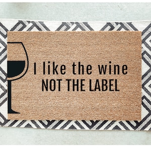 May include: A brown coir doormat with the text "I like the wine NOT THE LABEL" and a black silhouette of a wine glass.