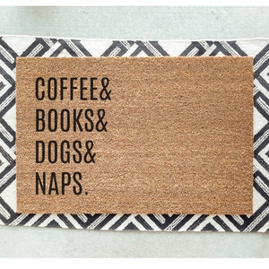 Op de afbeelding: Een bruine kokosmat met de tekst "COFFEE & BOOKS & DOGS & NAPS." in zwart gedrukt.