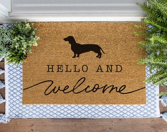 Könnte beinhalten: Eine braune Kokosmatte mit dem Text "Hello and welcome" und einer schwarzen Silhouette eines Dackels.