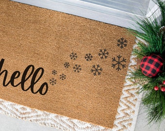 May include: A brown coir doormat with a white border and the word "hello" in black script. A trail of black snowflakes leads from the word "hello" to the top right corner of the mat.
