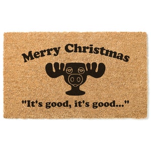 May include: A brown coir doormat with the text "Merry Christmas" and a black moose illustration. The text "It's good, it's good..." is printed below the moose.