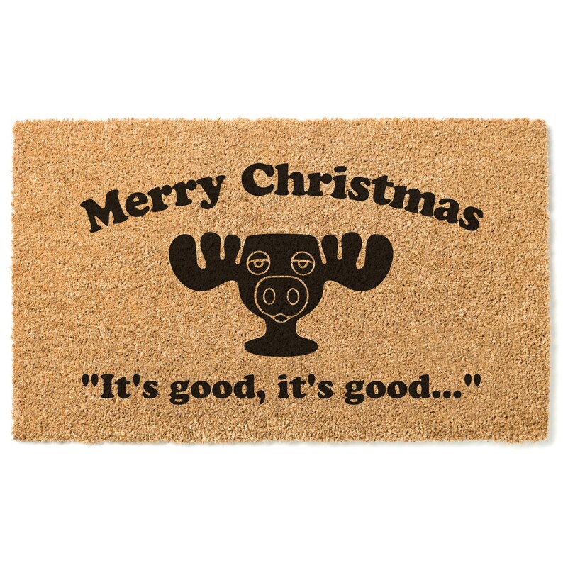 May include: A brown coir doormat with the text "Merry Christmas" and a black moose illustration. The text "It's good, it's good..." is printed below the moose.