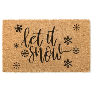 Peut inclure: Un paillasson en fibre de coco brun avec le texte "Let it snow" en lettres cursives noires. Le paillasson est d&eacute;cor&eacute; de plusieurs flocons de neige noirs.