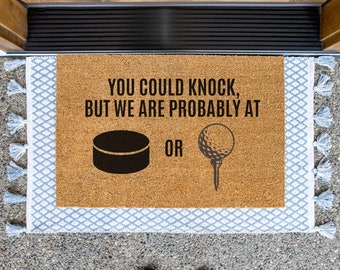 Puede incluir: Una alfombra de coco marrón con el texto "You could knock, but we are probably at" con un disco de hockey y una pelota de golf en tees a cada lado del texto. El texto "OR" está entre las dos imágenes.