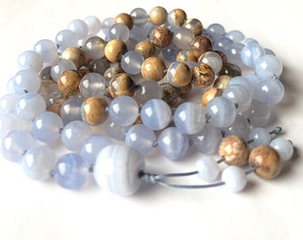 Könnte beinhalten: Eine blaue und braune Perlenkette mit einem geknoteten Quasten. Die Perlen sind aus Achat und sind eine Mischung aus hellblau und braun.