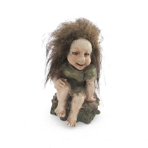 Op de afbeelding: Een grillig trollenbeeldje met een lachend gezicht, lang bruin haar en een groene jurk. De trol zit op een getextureerde, mosgroene basis, wat een charmant verzamelobject met fantasiethema creëert.