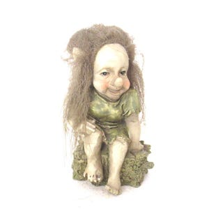 May include: A small, green-clad gnome figurine with a large, round head and a mischievous smile. The gnome is sitting on a tree stump with its legs crossed.