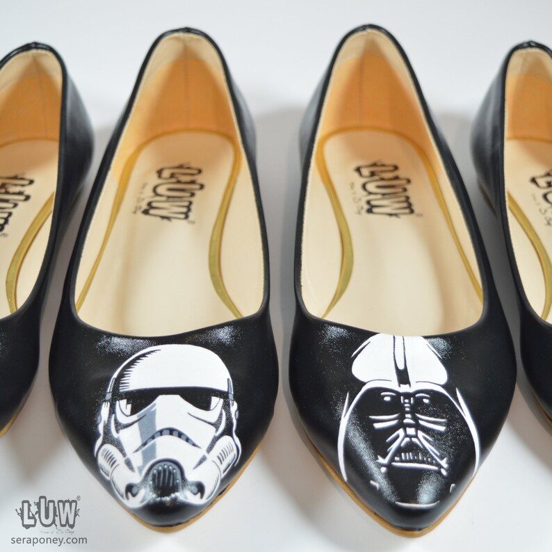 May include: Three pairs of black ballet flats with pointed toes. The flats are painted with Star Wars characters: Darth Vader, a Stormtrooper, and a TIE Fighter. The flats have a white interior and the word "LUW" printed on the inside.