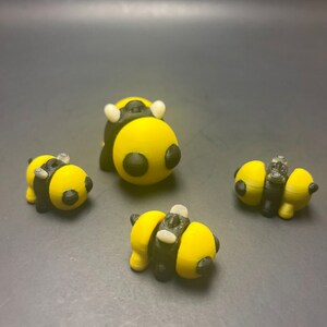 May include: Four 3D printed bumblebees in yellow and black. The bumblebees are in various poses, including standing, sitting, and flying.