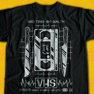 May include: Black t-shirt with a white graphic design of a VHS tape and two knives. The text "GOOD TIMES BAD QUALITY" is at the top of the design. The text "CAMP Z BLOOD 5" is on the VHS tape. The text "VHS VIDEO HORROR SOCIETY" is at the bottom of the design.