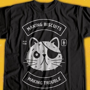 May include: Black t-shirt with a white graphic of a cat with an eye patch. The graphic says "Making Biscuits Making Trouble" and has a small fish icon.