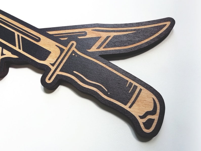 May include: Two black wooden knives with a light brown wood grain pattern. The knives are crossed over each other.