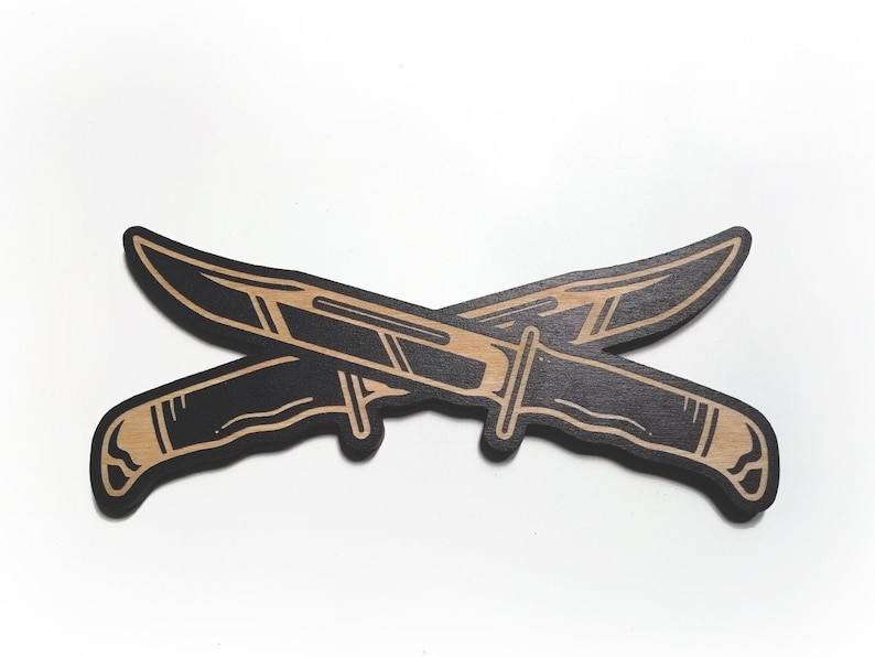 May include: Two black wooden knives with brown outlines are crossed over each other. The knives have a simple design with a blade and a handle.